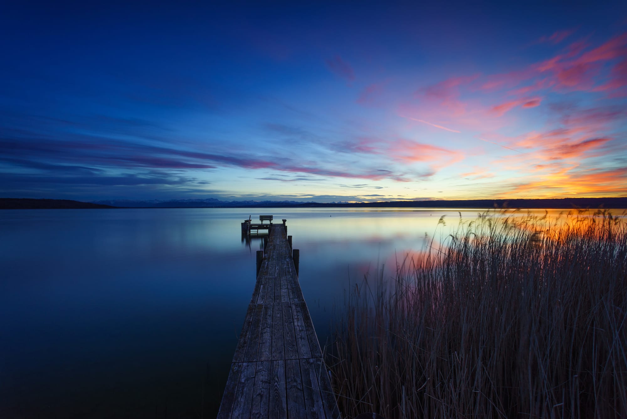 Panoramablick über den Ammersee mit bewaldetem Ufer und Alpenkette am Horizont